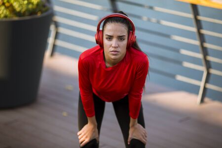 Pretty young sporty woman with earphones  taking break after a run in the urban environmentの写真素材