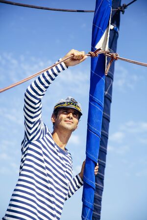 Handsome young man with captain cap on a sailboat at sea on a suuny day