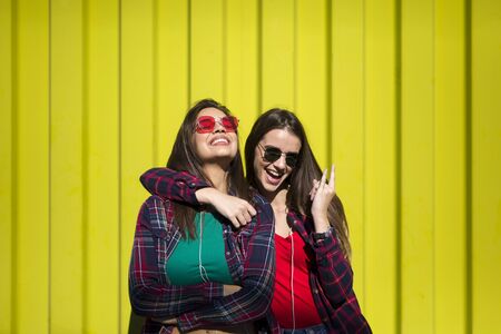 Image of two young happy women friends standing outdoor over yellow wallの写真素材