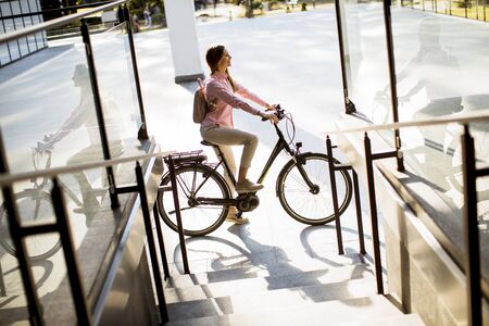 Pretty young woman with modern city electric e-bike clean sustainable urban transportationの写真素材