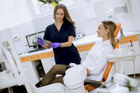 Pretty young female doctor with protective gloves examining radiograph with her patient in the dentist officeの写真素材