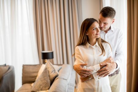 Young couple embracing standing in living room of a contemporary apartmentの写真素材