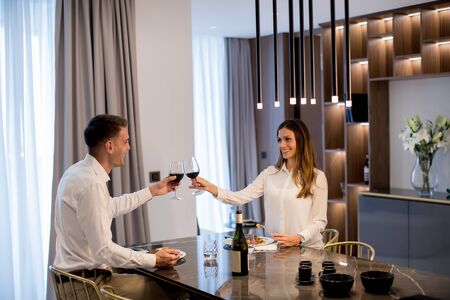 Sweet young couple having a romantic dinner and toasting with glasses of red wine at luxury kitchenの写真素材