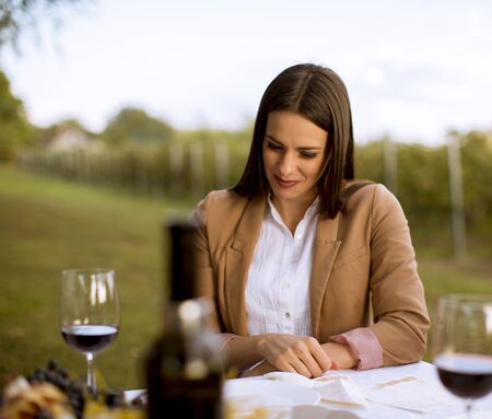 Attractive stylish young woman drinking glass of red wine in vineyard