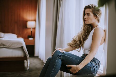 Beautiful young woman sitting by the window in apartmentの写真素材