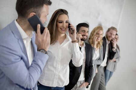 Group of young people with mobile phones standing by the grey wall