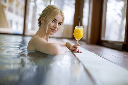 Pretty young blonde woman relaxing on the poolside with glass of orange juiceの写真素材