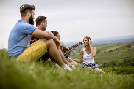Group od young people sitting on grass and having fun on a field trip in nature on a mountain
