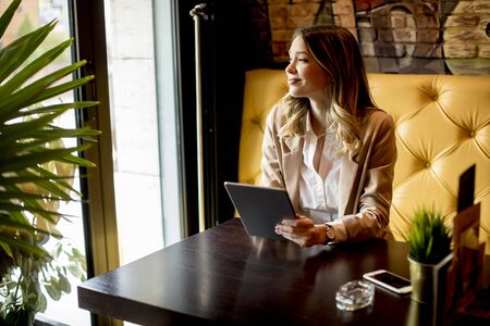 Smiling charming young woman with digital tablet sitting in cafeの写真素材