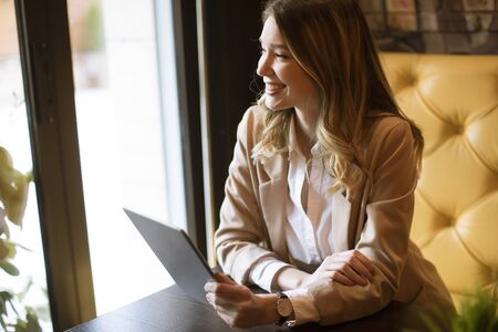 Smiling charming young woman with digital tablet sitting in cafeの写真素材