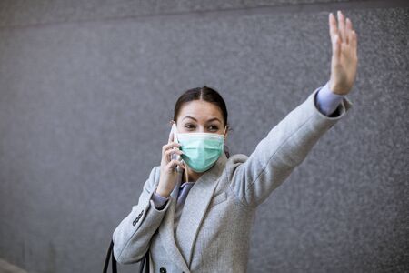Pretty young woman with protective facial mask on the street using mobile phone