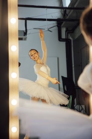 Young ballerina in white dress with a perfect body is dancing in front of the mirrorの写真素材