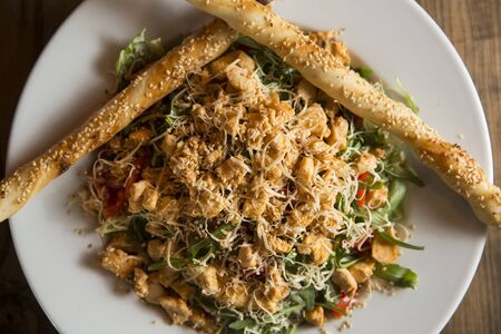 Chicken salad with rocket, cherry tomatoes, smoked cheese and crunchy sesame sticks in the plate on the wooden tableの写真素材