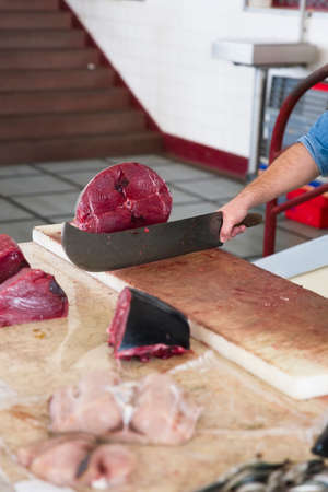 FUNCHAL, PORTUGAL - FEBRUARY 15, 2020: Unidentified man cutting tuna Mercado dos Lavradores (Farmers market) in Funchal at Madeira Island, Portugal. Market building was designed by Edmundo Tavares and opened at 1940.のeditorial素材