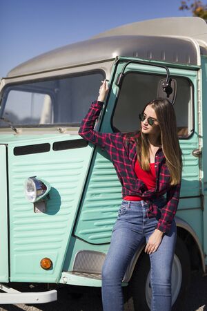 Smiling pretty young woman standing by the vintage minivanの写真素材