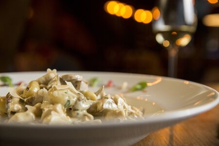 Gnocchi with turkey meat and porcini mushrooms in a cream sauce on the plate with glass of white wineの写真素材