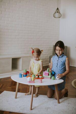 Two cute little girls play with blocks at the table in the roomの写真素材
