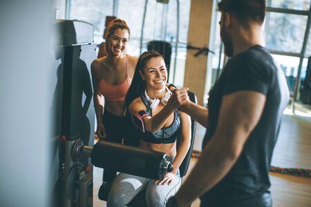 Pretty young woman having exercises on leg extension and leg curl machine in the gym