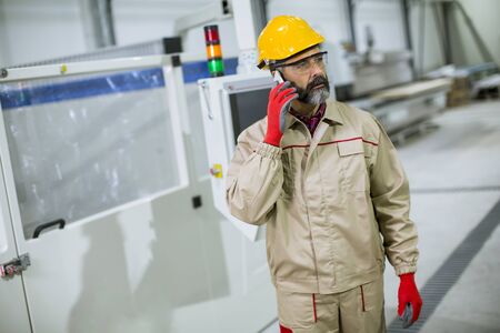 Portrait of mature industrial man engineer with smartphone in a factory
