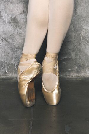 Closeup of legs of the young ballerina with pointe shoes by the grunge wall