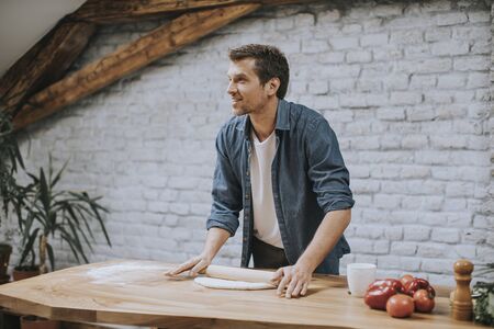Handsome young man making dough in the rustic kitchen