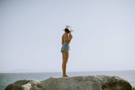 Pretty young woman in bikini standing on rocks by the seaの写真素材