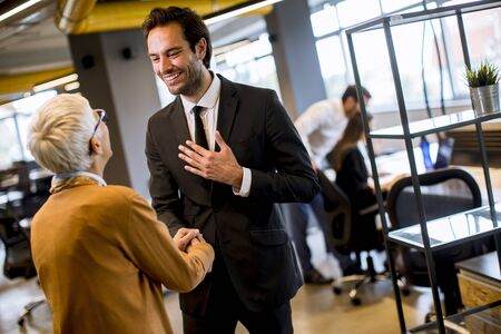 Young business man and senior business woman shaking hands in the modern office