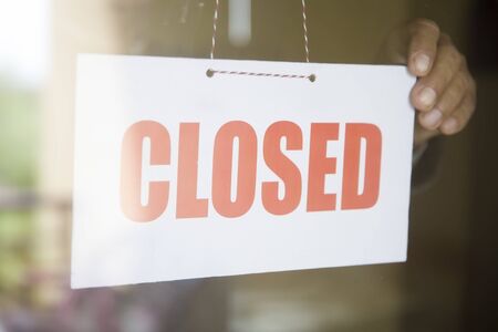Business store owner turning closed sign at glass shop doorwayの写真素材