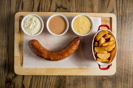 Sausage and potatoes with sauces on the wooden plateの写真素材
