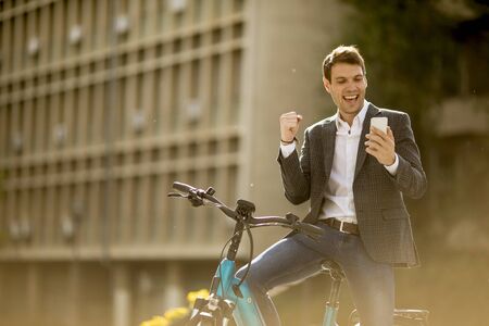 Handosme young businessman on the ebike received gret news by mobile phoneの写真素材
