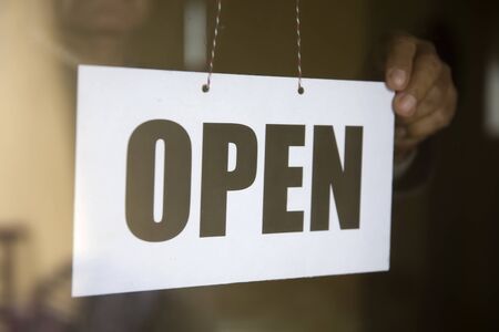 Close up of the business owner hanging an open sign at a glass door