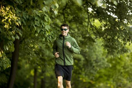 Athletic handsome young man running while doing workout in sunny green parkの写真素材