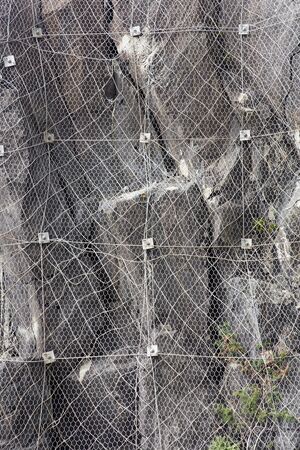 Closeup of slope of the mountain with a rockfall protection net preventing rocks falling on the roadの写真素材