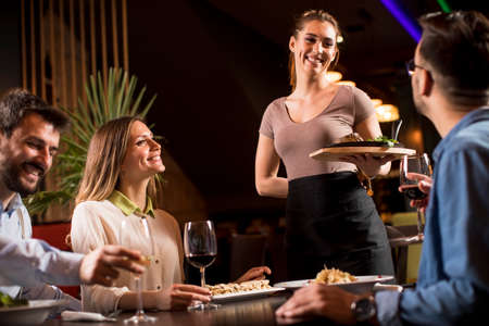 Pretty waiter woman serving group of friends with food in the restauraの写真素材