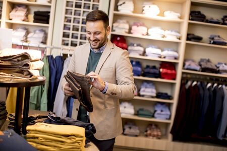 Handsome young man buying trousers in the store