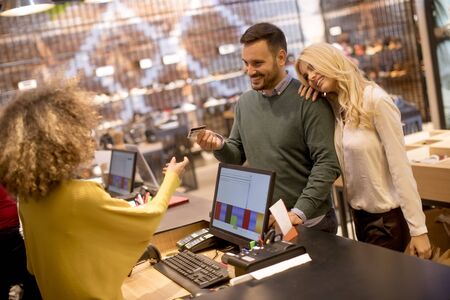 Handsome young man paying female sales assistant with credit card in clothes shopの写真素材