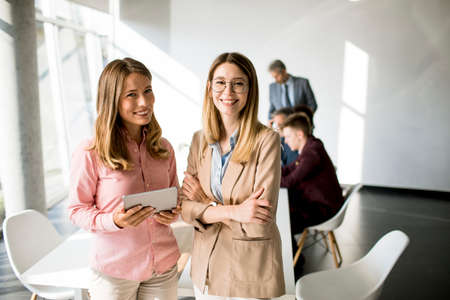Two smiling young women looking on digital tablet at the officeの写真素材