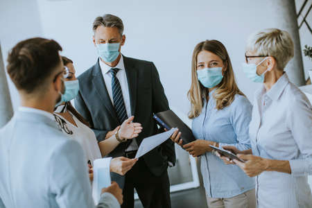 Business partners standing and looking at business results in the office while wearing face masks sa...