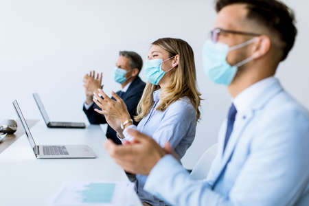 Group of business people with protection masks clapping hands after successful business meeting in...