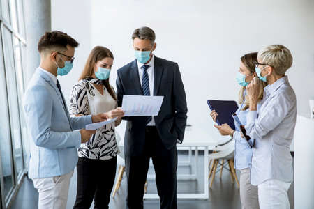 Business partners standing and looking at business results in the office while wearing face masks sa...
