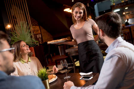Pretty waiter woman serving group of friends with food in the restaurantの写真素材