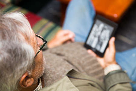Senior man using an ebook reader in the sofa