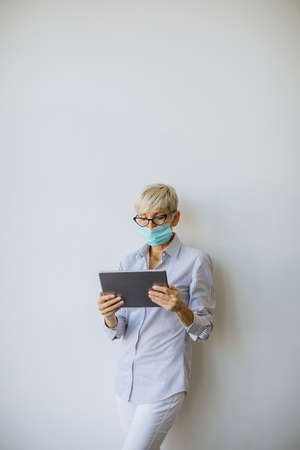 Mature businesswoman using a handheld digital tablet and wear mask to prevent infection by corona virusの写真素材