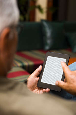 Senior man using an ebook reader in the sofa