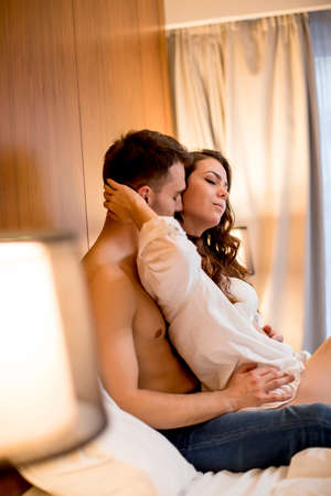 Loving and hugged young couple sitting on the bed in the bedroom