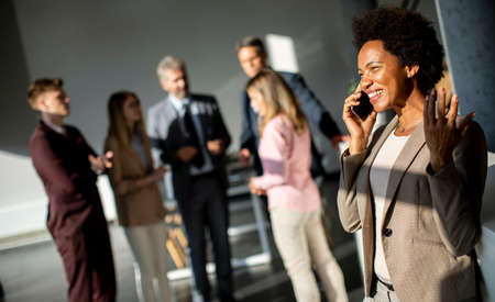 Young African American businesswoman standing and using mobile phone in the modern officeの写真素材
