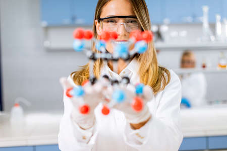 Female chemist with safety goggles hold molecular model in the labの写真素材
