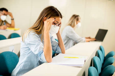 Young female student wearing face protective medical mask for virus protection at lecture hallの写真素材