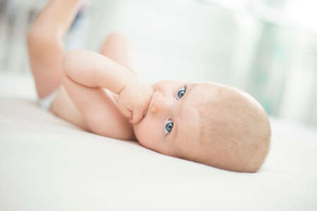 Cute little baby girl lying with hand in mouthの写真素材