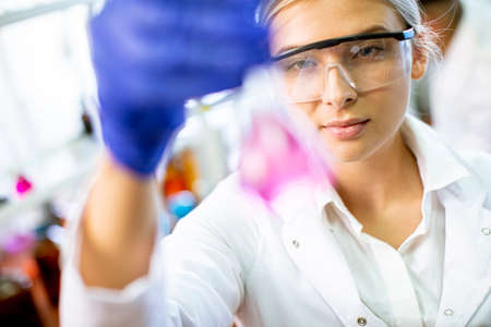 Pretty young female scientist examining liquid in biochemical lab